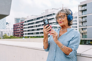Senior woman using smartphone with headphones in urban setting