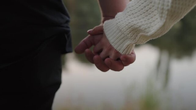 Close-up shot of a couple holding hands, capturing a moment of intimacy and connection during a serene outdoor walk. Couple Holding Hands Gently on a Romantic Walk Outdoors