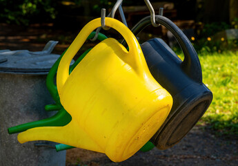 colorful plastic watering cans hanging on metal hooks in sunlight in a garden