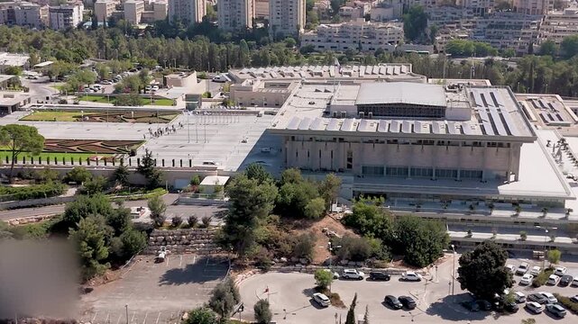 Aerial view of The Knesset government building surrounded by vibrant green trees and structured landscaping, creating a stark contrast with the urban environment, Jerusalem, Israel.