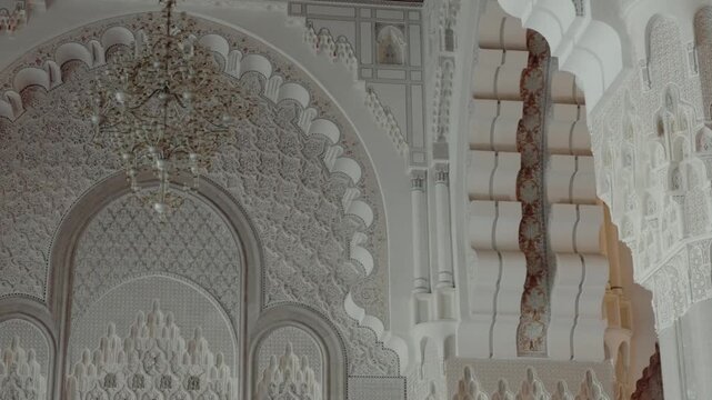 Ornate Moroccan architecture with intricate details. White walls, arches, and a chandelier. Cultural heritage, mosque, Islamic art, craftsmanship, and elegance. Architectural details, Moroccan design