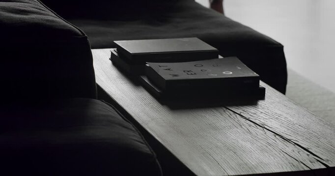 Close up delails in a Modern contemporary Minimalist living room with black furniture and wooden table and books. The man walks next to the table and creates silhouettes and shadows.