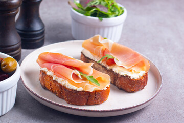 Two bruschettas with prosciutto, ricotta cheese and rucola on ciabatta bread. Olive and spices  decorated.