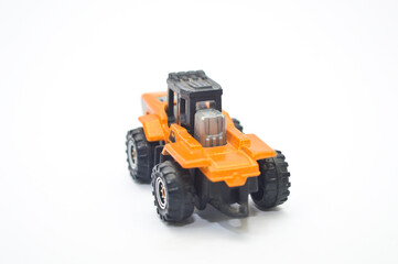 Close-up of a well-worn orange and black die-cast toy tractor, construction vehicle, isolated on a white background. Represents childhood, engineering, industry, play, and transportation concept.