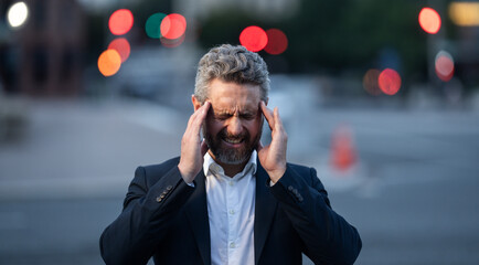 Tired business man suffering from a headache in night city. Man relieving pain from migraine. Financial problems and stress. Business crisis and bankruptcy concept. Business man worried and stressed.
