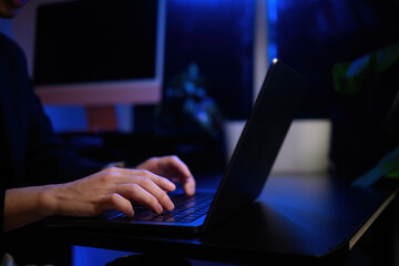 Close-up of a person typing on a laptop keyboard late at night under blue lighting, representing focus, work, technology, and productivity
