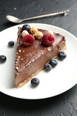 Piece of delicious chocolate cheesecake with nuts, berries and spoon on black table, closeup