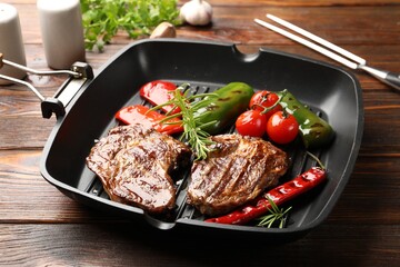Pan with grilled beef steaks, rosemary and vegetables on wooden table, closeup