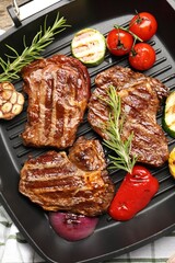 Pan with grilled beef steaks, rosemary and vegetables on table, top view