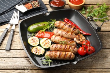 Pan with grilled sausages, vegetables, spices and sauces on wooden table, closeup