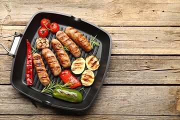 Pan with grilled sausages, vegetables and spices on wooden table, top view. Space for text