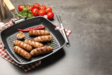 Pan with grilled sausages, spices and tomatoes on gray textured table, closeup. Space for text
