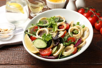Delicious salad with squid rings and vegetables served on wooden table, closeup
