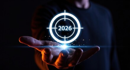 A hand holds a glowing target symbol with the year 2026, goals future aspirations in a dark background.