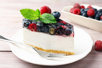 Piece of delicious cheesecake with berries, mint and fork on wooden table, closeup