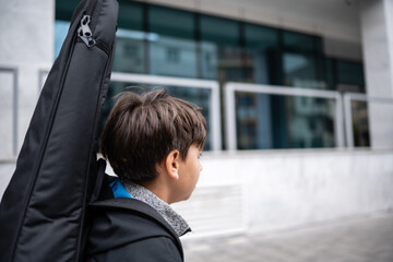 Young boy carrying a guitar case walking