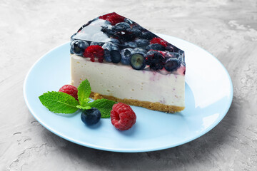 Piece of delicious cheesecake with berries and mint on grey table, closeup