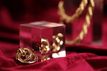 Stylish gold jewelry on red cloth, closeup. Space for text