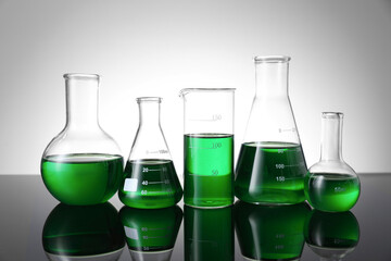 Different laboratory glassware with green liquid on table against white background