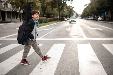 Young musician boy walking with guitar at crosswalk
