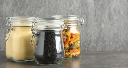 Glass jars with different products on grey table, closeup. Space for text