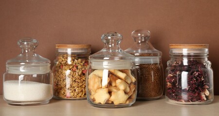 Glass jars with different products on wooden table against brown background