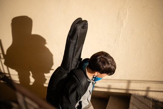 Young musician carrying guitar case walking downstairs