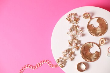 Stylish presentation of beautiful gold jewelry on pink background, top view. Space for text