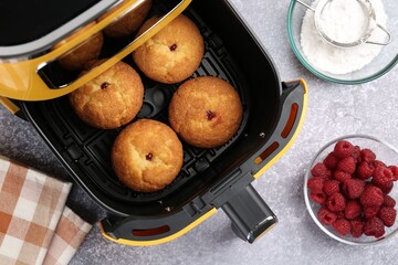 Freshly baked muffins in air fryer and ingredients on grey textured table, flat lay