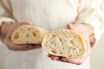 Woman holding halves of fresh ciabatta on light background, closeup