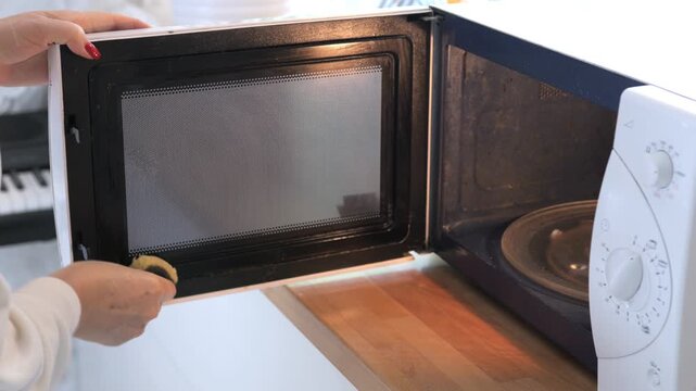 Woman is opening a microwave oven. The microwave is black and white. The microwave door is open