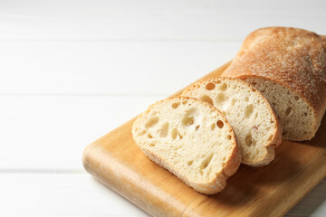 Cut crispy ciabatta on white wooden table, closeup. Space for text