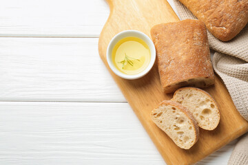 Fresh crispy ciabattas and oil with rosemary on white wooden table, flat lay. Space for text