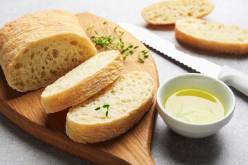 Fresh crispy ciabatta, herbs and oil on grey table, closeup
