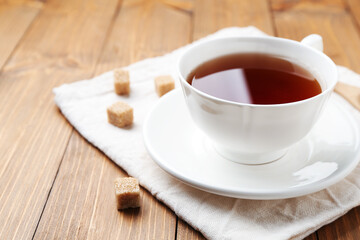 Aromatic black tea in cup and sugar cubes on wooden table, closeup. Space for text