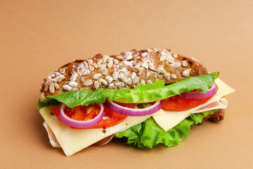 Tasty ciabatta sandwich with cheese and vegetables on brown background, closeup
