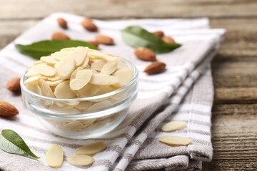 Fresh almond flakes and whole nuts on wooden table, closeup. Space for text
