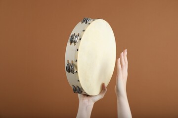 Woman playing tambourine on brown background, closeup