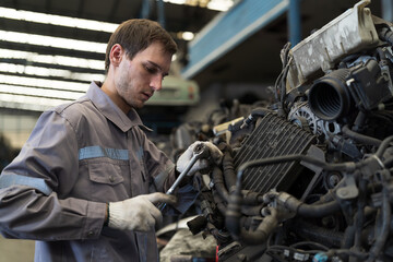 Male auto mechanic working, using socket wrench tighten old engine nuts for separate parts in warehouse auto spare parts. Car service technician check and repair car engine in garage