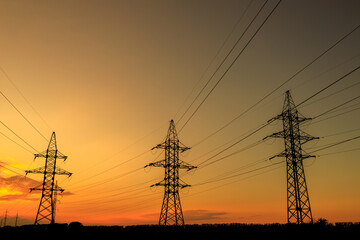 Silhouettes of three tall power lines loom against the backdrop of a beautiful sunset