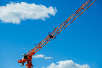 An orange construction tower crane on a blue sky background