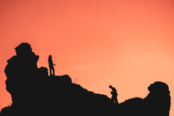 silhouettes of two people against the sunset, a man carrying a stone, a woman standing on top and waiting