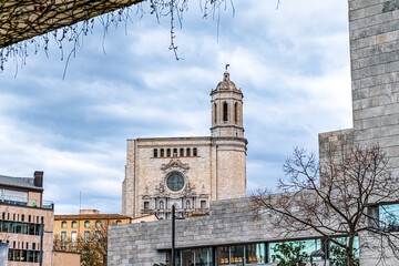 Girona Cathedral with its baroque facade rising above modern city buildings. Architectural contrast between historic religious landmark and contemporary urban structures under cloudy sky in Spain