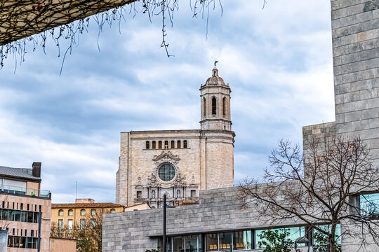 Girona Cathedral with its baroque facade rising above modern city buildings. Architectural contrast between historic religious landmark and contemporary urban structures under cloudy sky in Spain