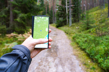 Hand holding smartphone with GPS navigation app on forest trail, hiking and outdoor orientation