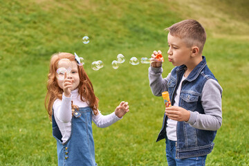 Fototapeta premium Caucasian children playing with bubbles outdoors on a sunny day in a park.