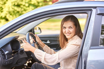 Naklejka premium Smiling caucasian female adult driving a car with open door in sunny outdoor setting.