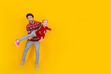 Father joyfully playing with his daughter in vibrant Christmas apparel against a yellow background, spreading holiday cheer