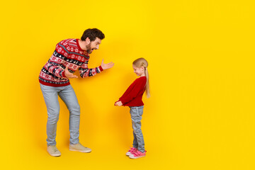 Single father and daughter bonding playfully in Christmas sweaters against a vibrant yellow background during the festive season
