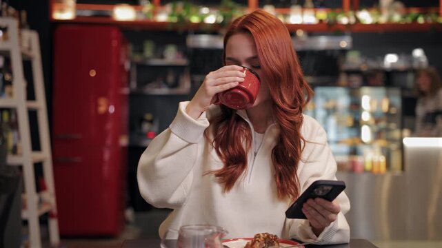 Peaceful female dressed in white sipping warm drink with eyes closed. Holding smartphone in hand. Reading news or scrolling social media while enjoying break during quiet cafe visit.